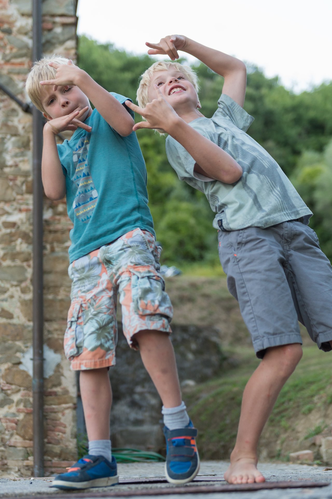 Two children strike playful dance poses, making hand gestures and smiling during an outdoor gathering.