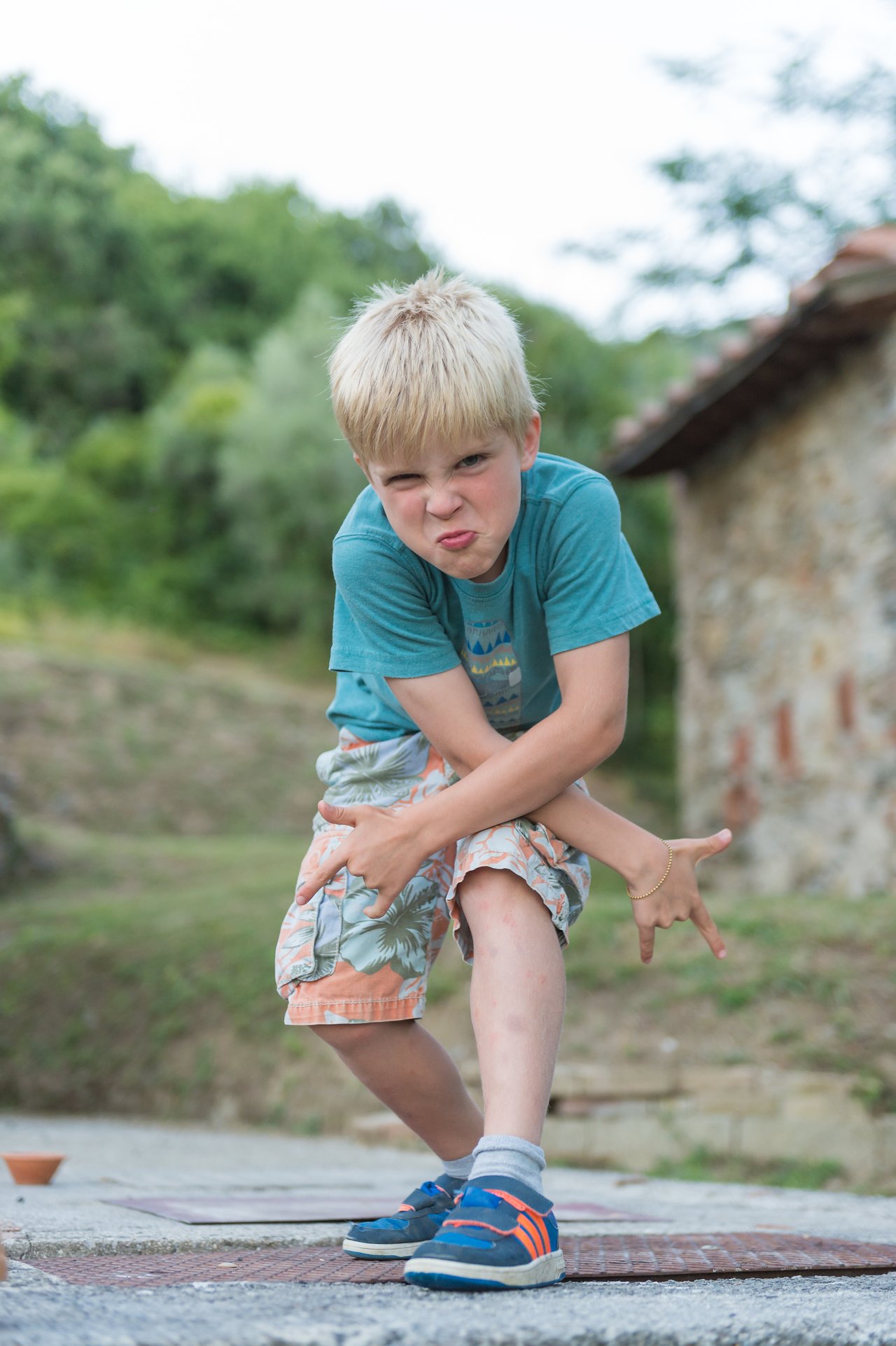 A young boy strikes a playful dance pose, crossing his arms and making hand gestures with a determined expression.