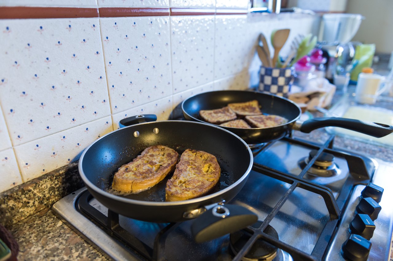 Slices of French toast cooking in two frying pans on a gas stove in a kitchen.