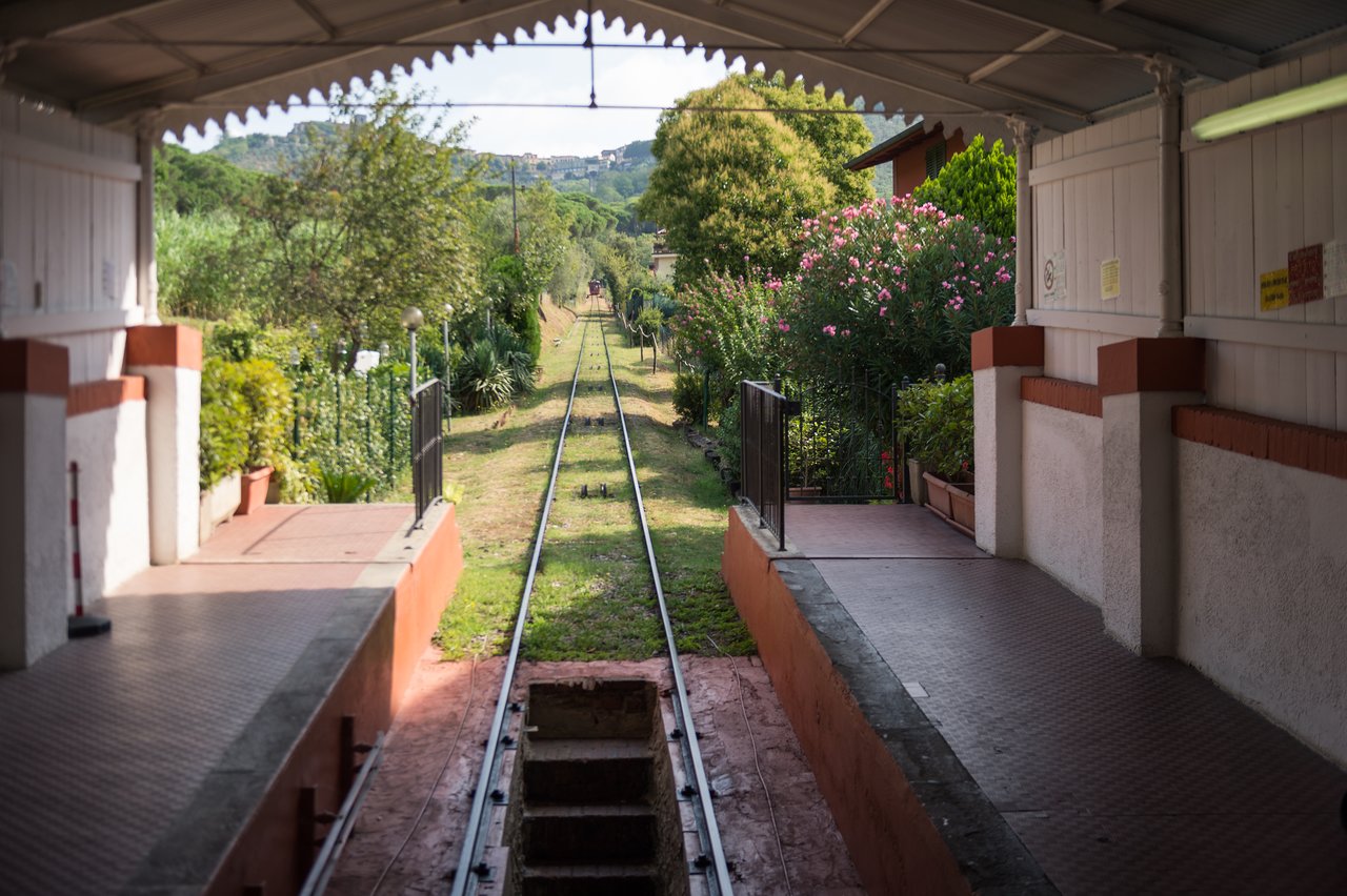 A funicular railway track leading into the distance from a small station with a covered platform and greenery.