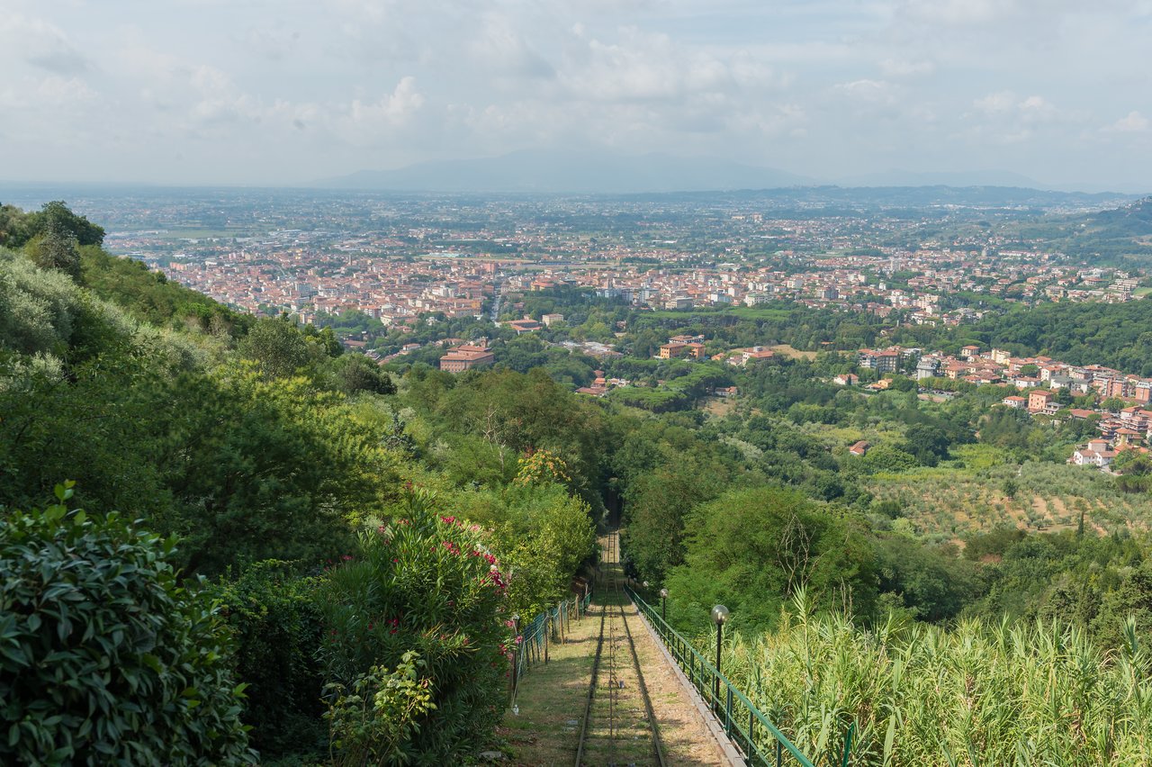 Funicular railway tracks descend through green hills, overlooking a cityscape in Montecatini Alto, Tuscany.