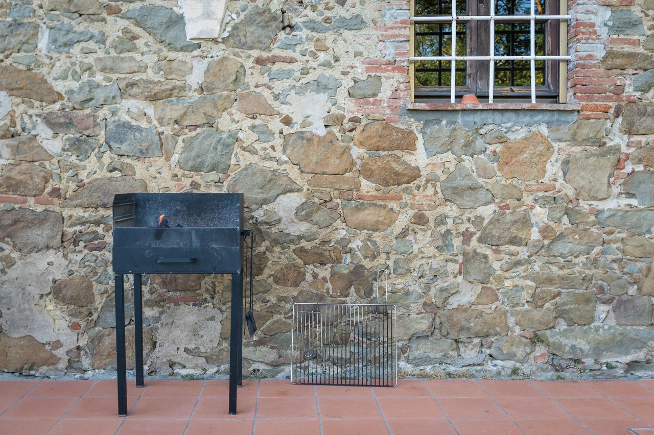 A black metal grill with a grate leaning against a stone wall on a tiled patio.