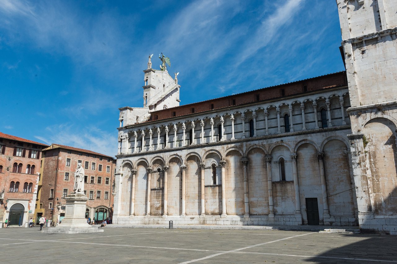 A historic church with arched columns and a statue in a public square in Lucca, Italy.