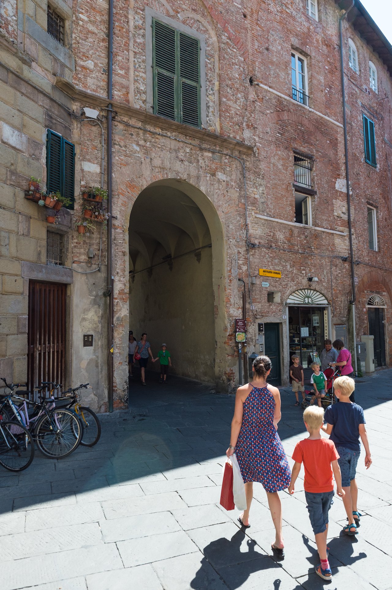 A woman and two children walk toward an arched entrance in a historic brick building in Lucca, Italy.