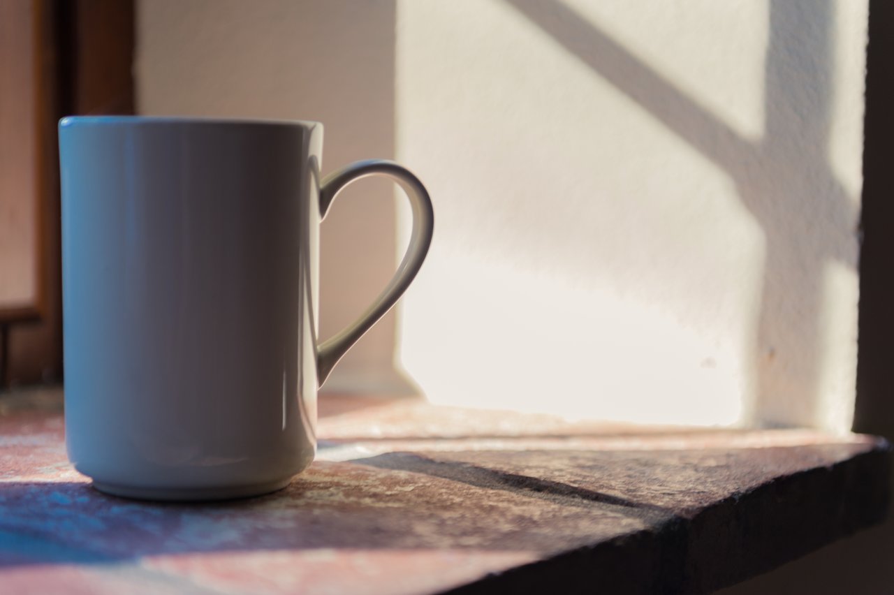 A white mug sits on a sunlit windowsill, casting a shadow on the wall behind it.