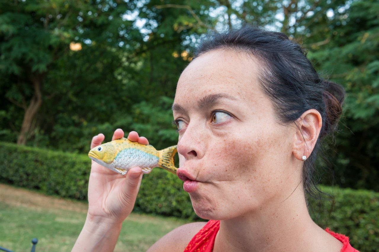 A woman playfully puckers her lips while holding a small fish figurine close to her face.