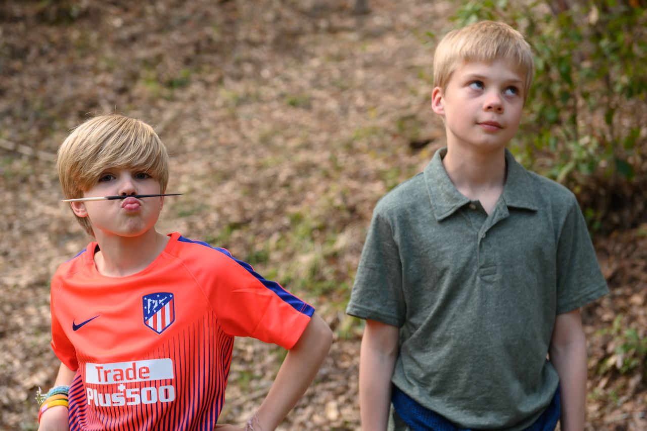 One child makes a playful face with a porcupine needle under his nose, while another looks away with an eye roll.