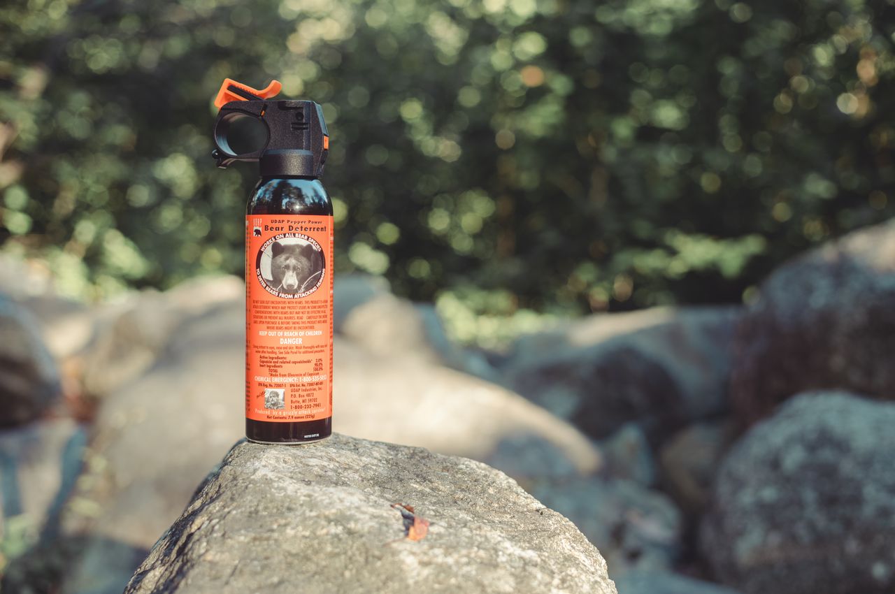 A can of bear spray sits on a rock in a wooded area, ready for use in case of bears.