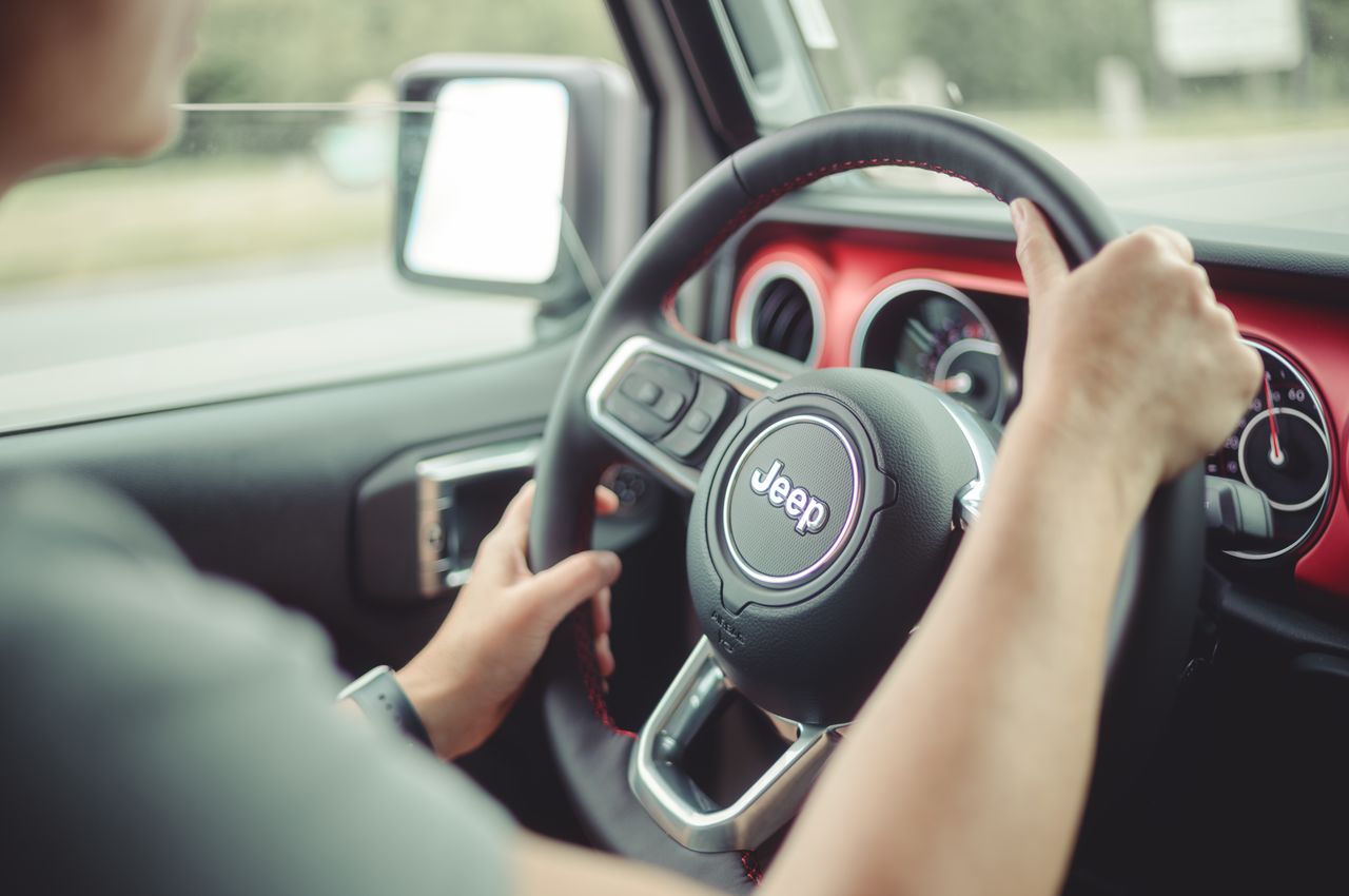 A person is driving a Jeep, holding the steering wheel with both hands.