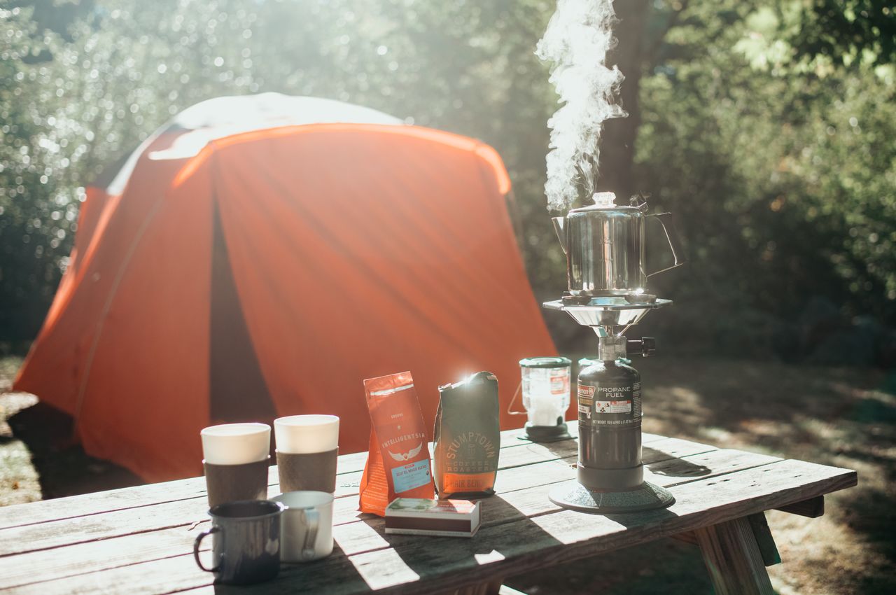 An aluminum moka pot brewing on a camping stove, with our orange tent in the background.