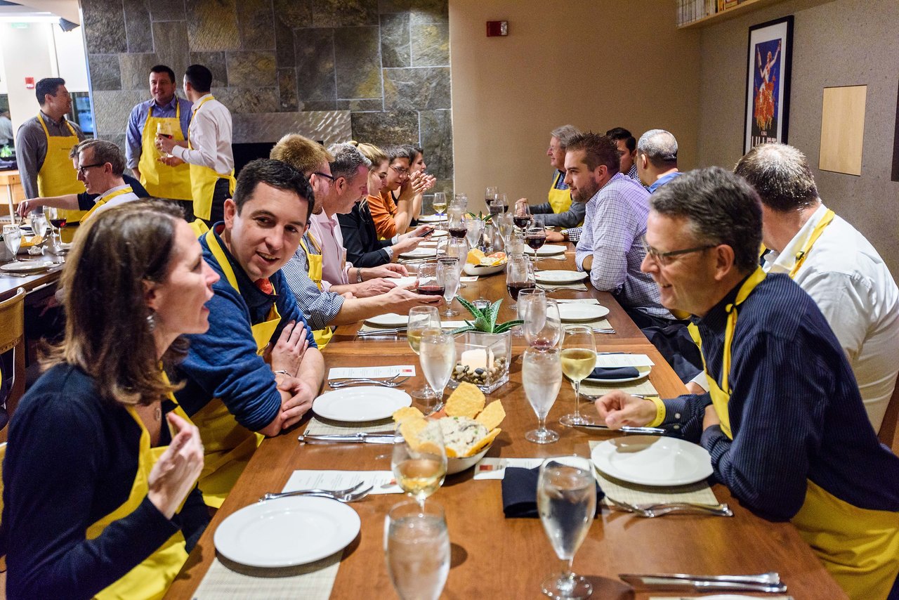 A group of people wearing yellow aprons sit at a long table, talking and enjoying a meal together.