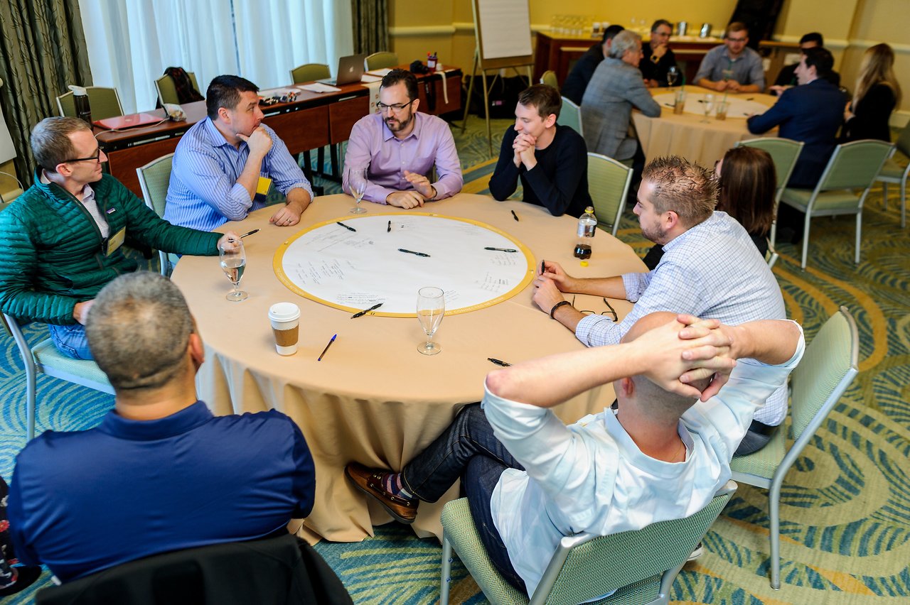 A group of people sits around a table, discussing and writing on a large paper during a workshop.