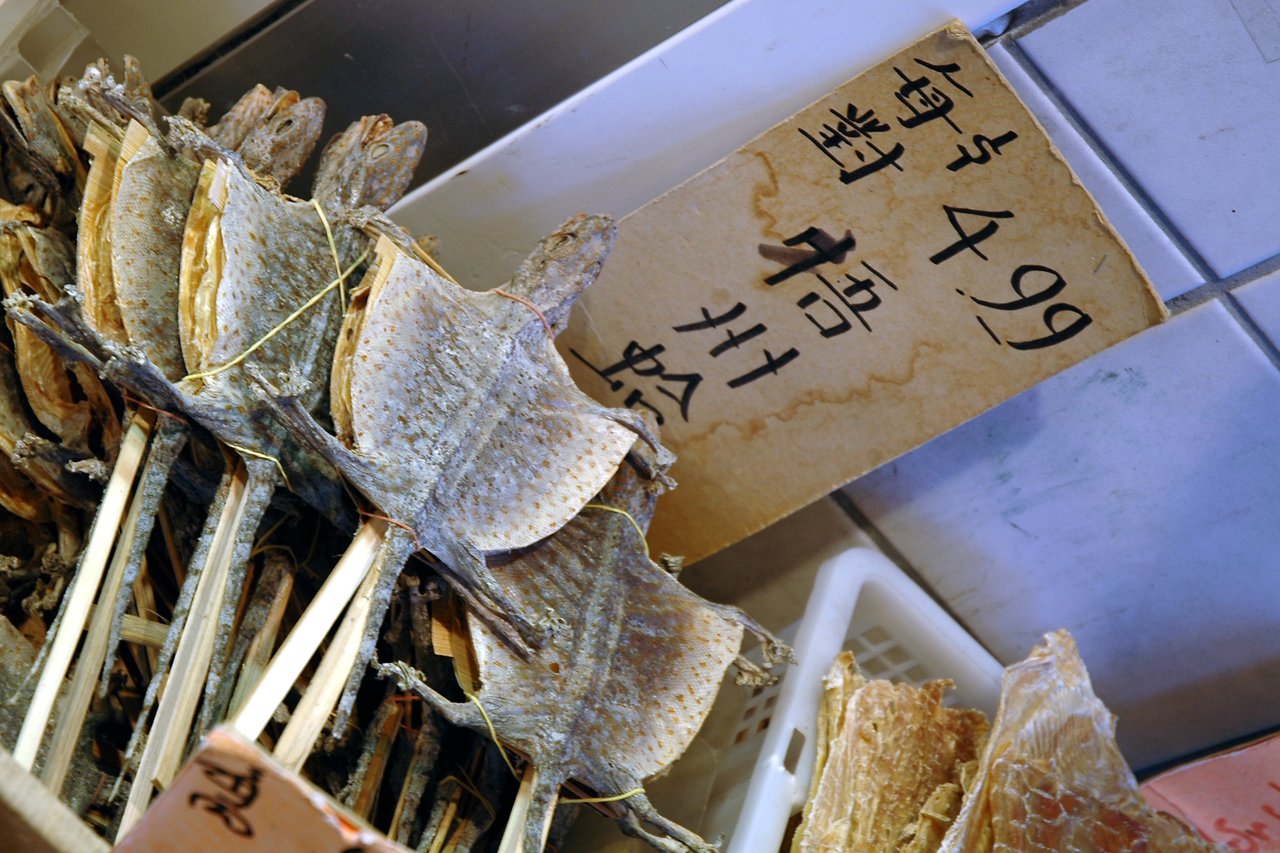 Dried fish on sticks displayed for sale with a handwritten price sign in Chinese characters.