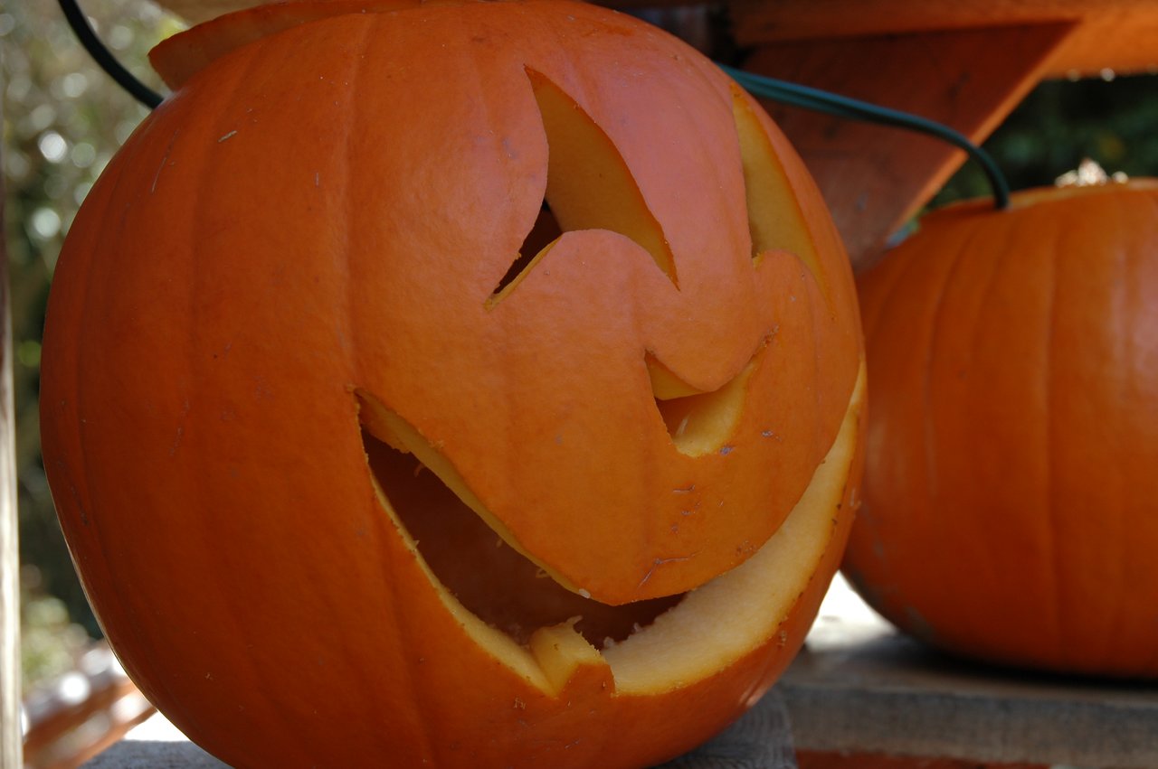 A carved pumpkin with a smiling face sits on a surface, with another uncarved pumpkin in the background.