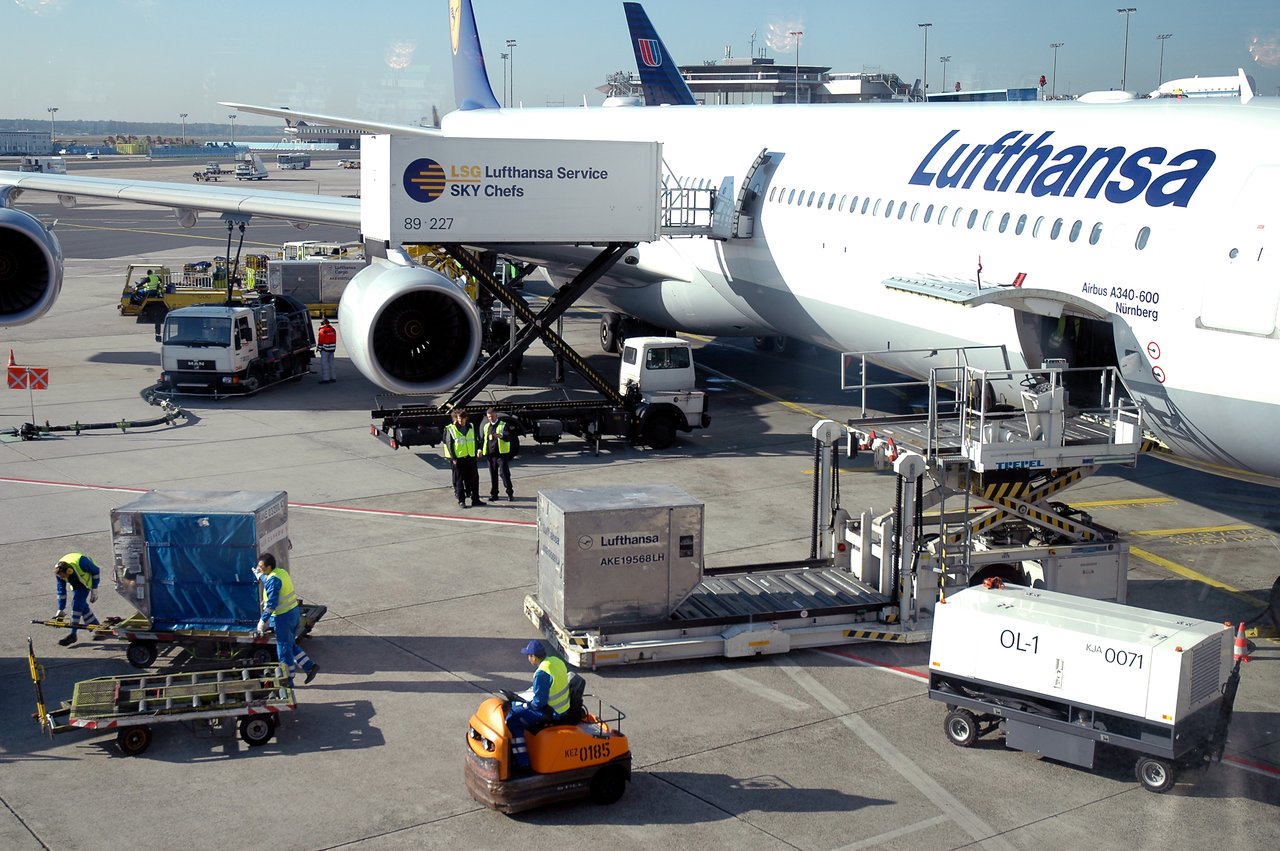 Airport workers load cargo and prepare a Lufthansa airplane for departure at the gate.