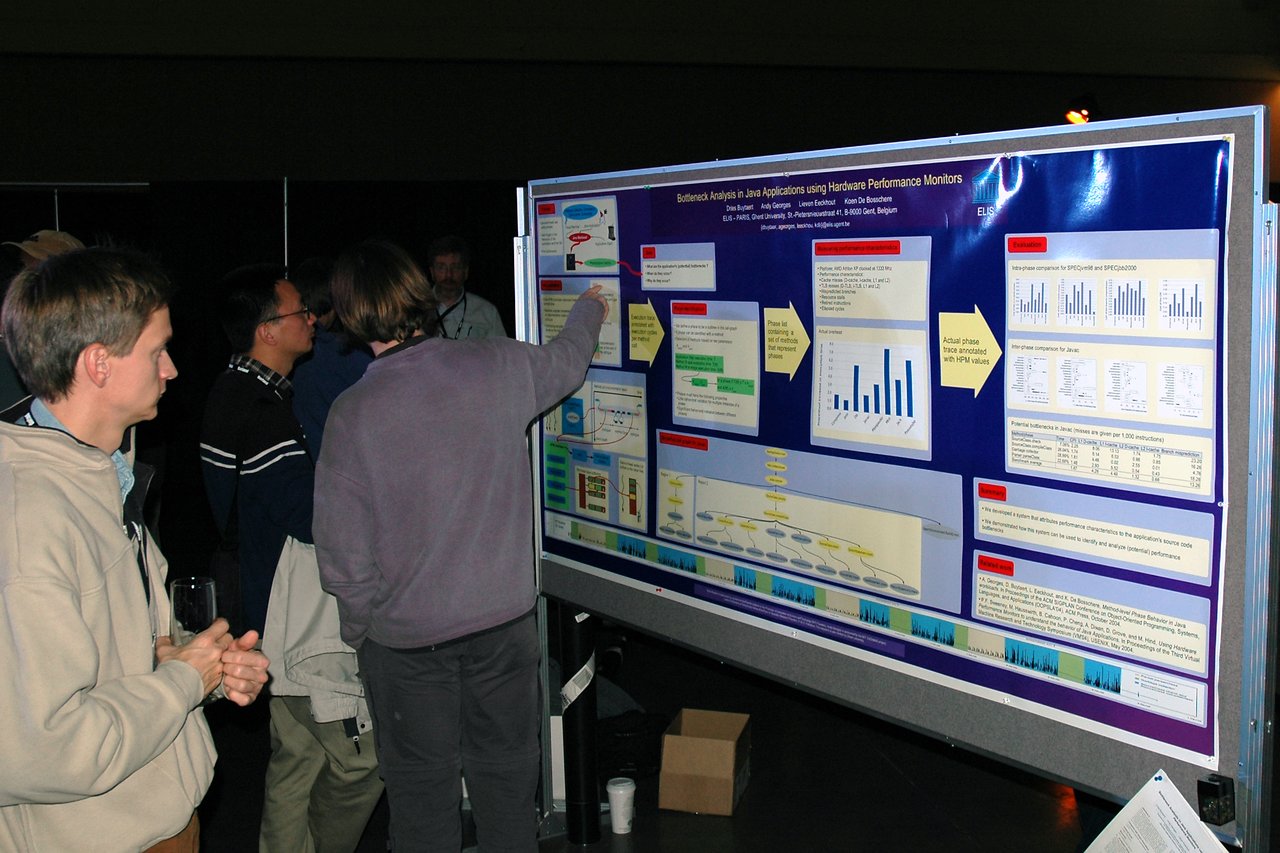 A person points at a research poster while others listen and observe during a conference poster session.
