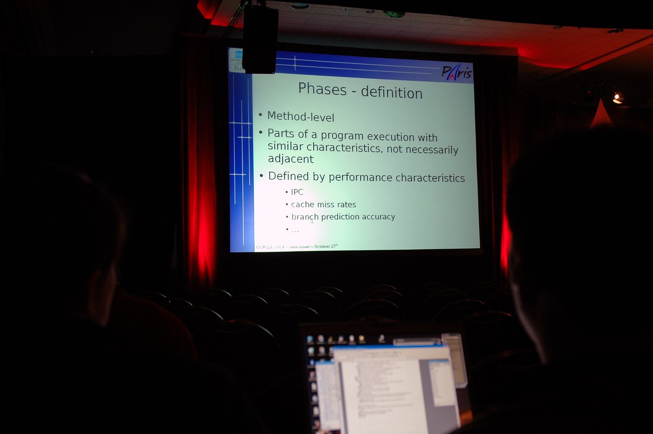 A person watches a presentation on program execution phases while working on a laptop in a dimly lit room.