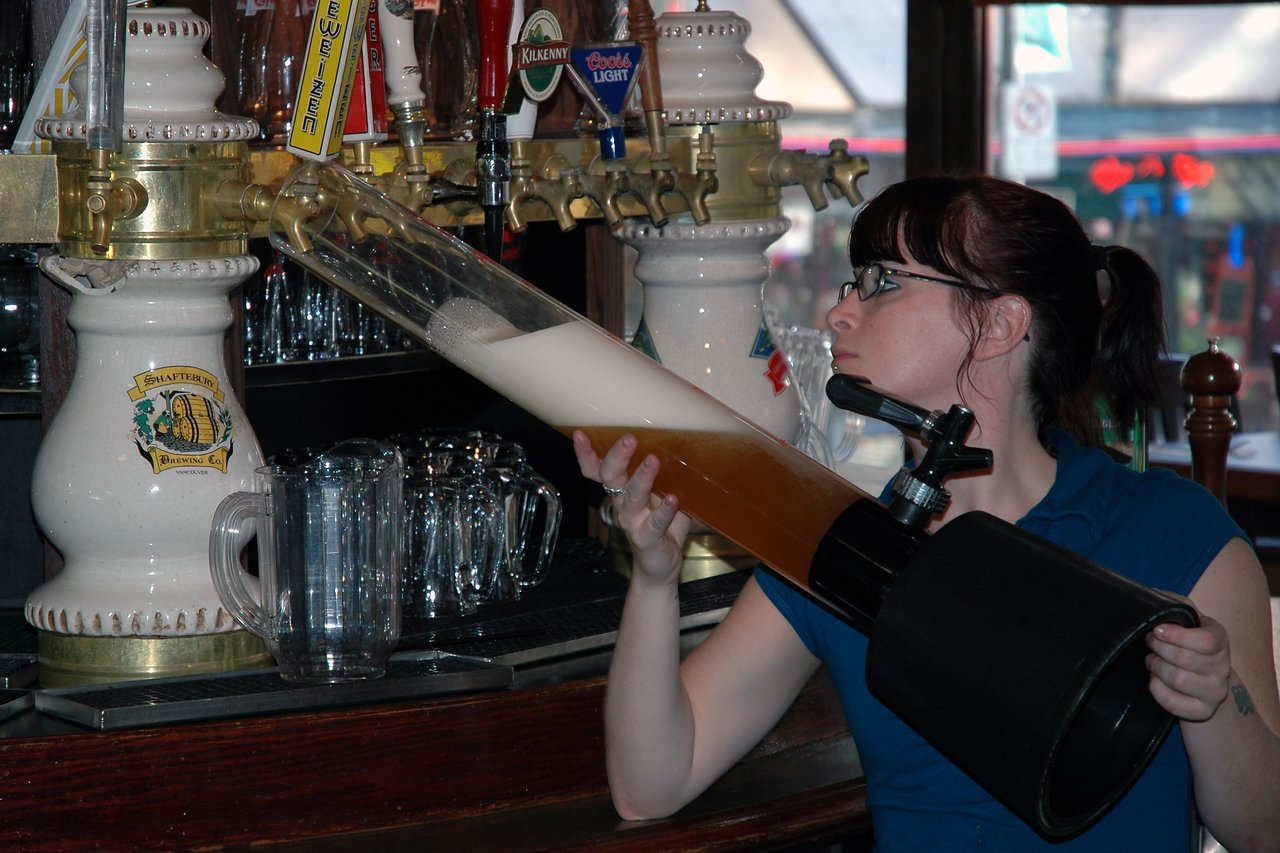 A bartender fills a large beer tower from a tap at a pub.