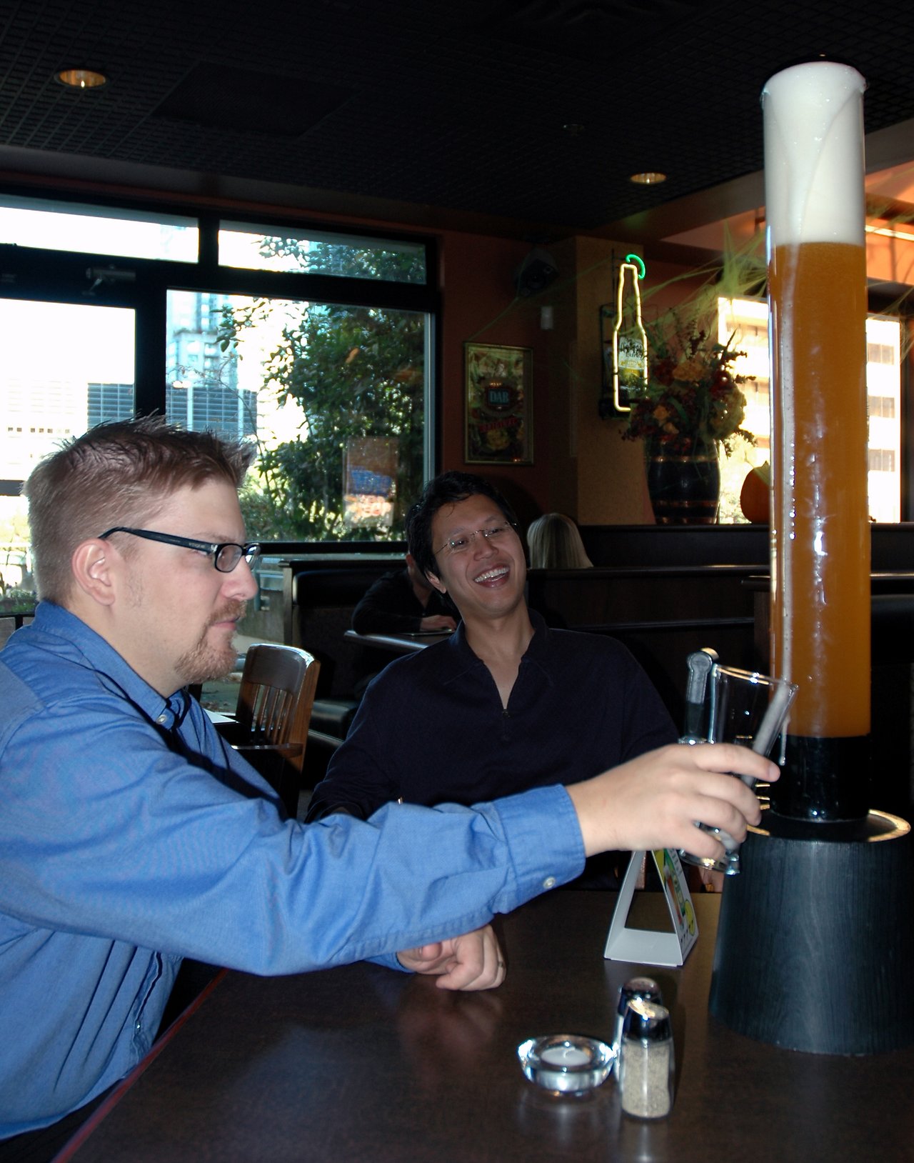 Two people at a pub pouring beer from a tall beer tower into a glass while smiling and enjoying the moment.