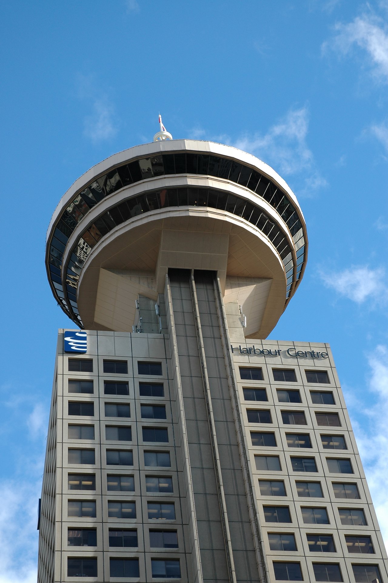 The Vancouver Harbour Centre building with its round observation deck, viewed from below against a blue sky.