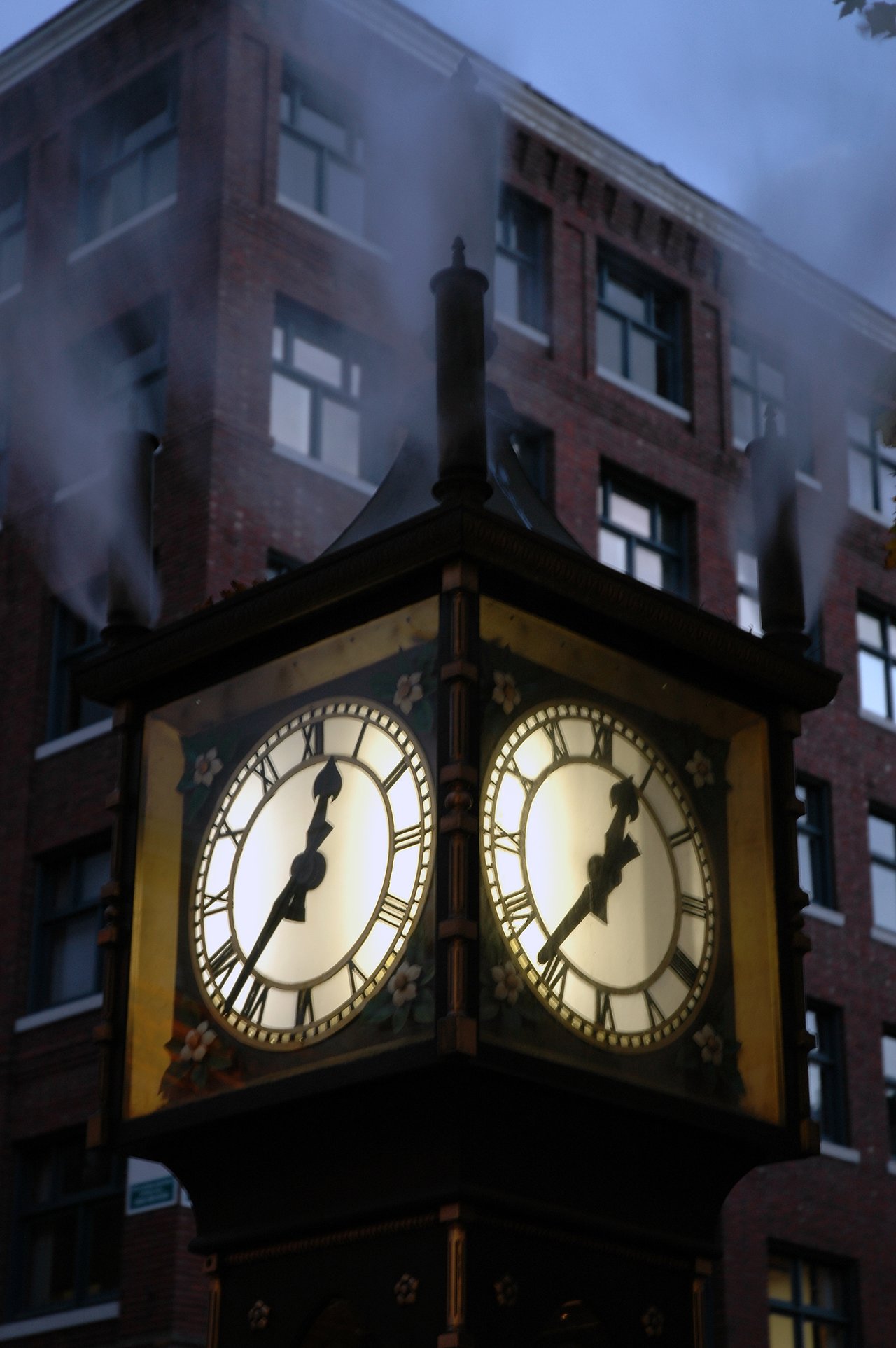 A steam-powered clock in Vancouver releases steam from its vents, with illuminated clock faces showing the time.