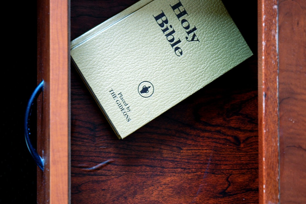 A Holy Bible placed inside a wooden hotel nightstand drawer.