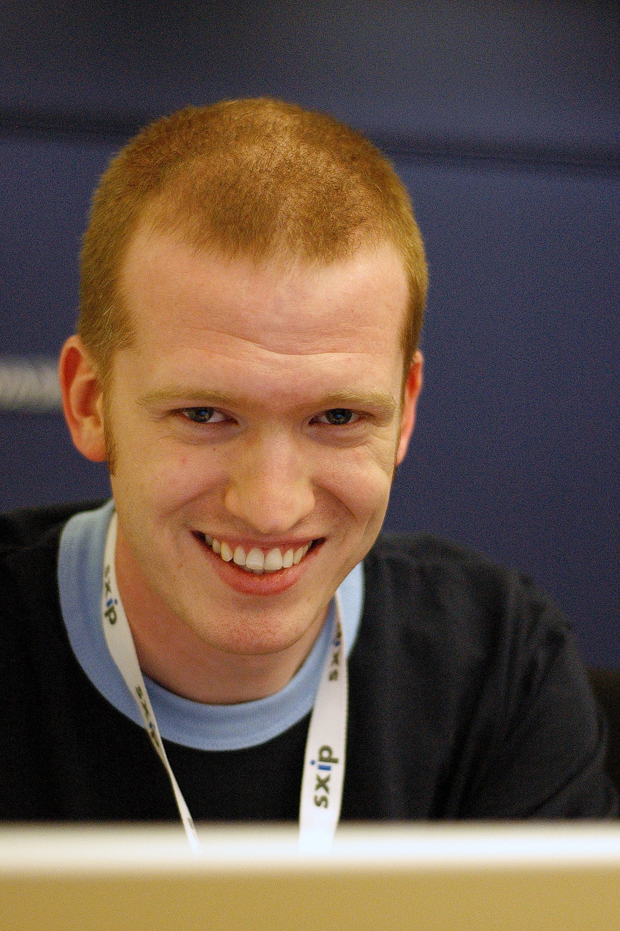 A man wearing a lanyard smiles while looking at a screen.