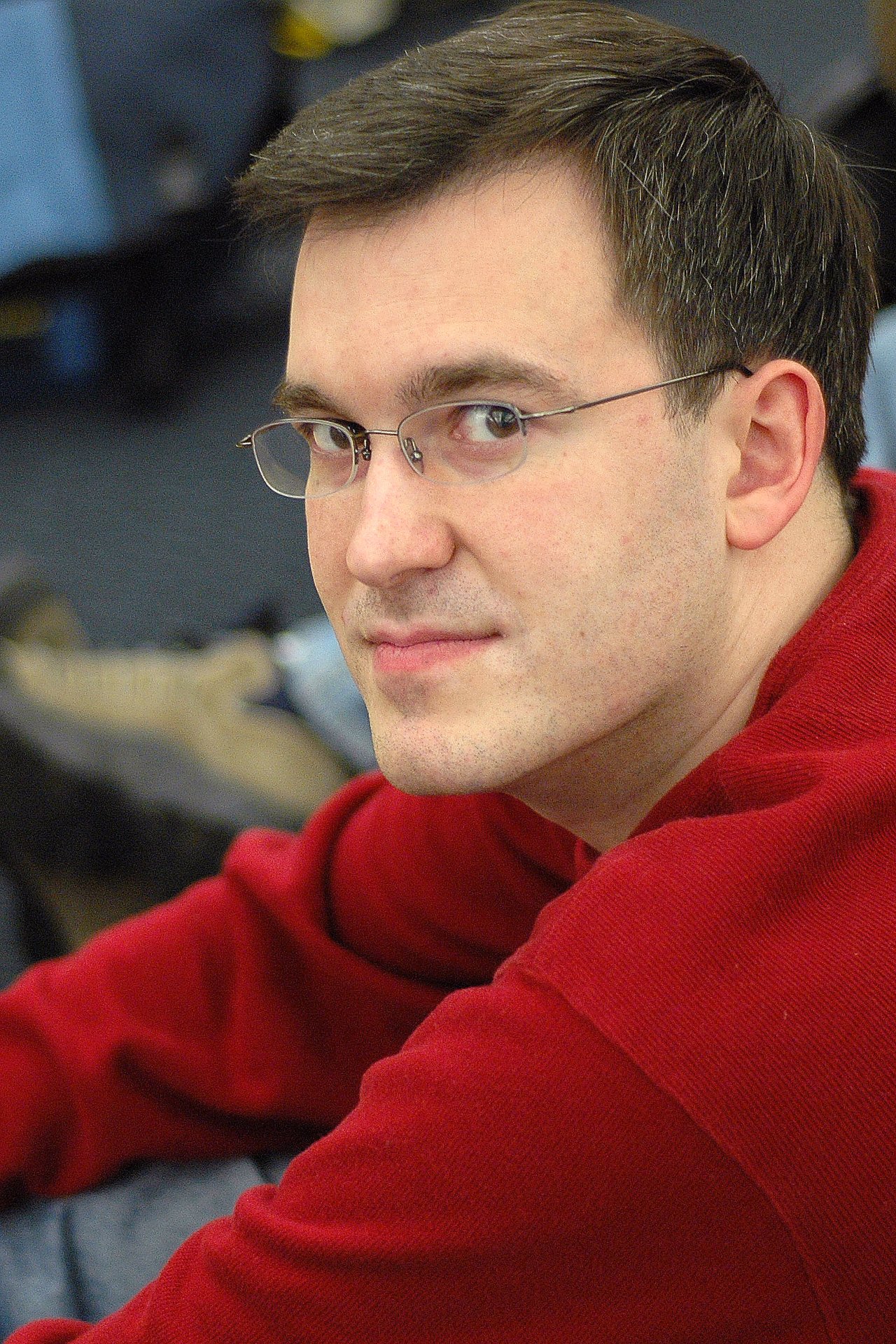 A man wearing glasses and a red sweater looks at the camera with a slight smile.