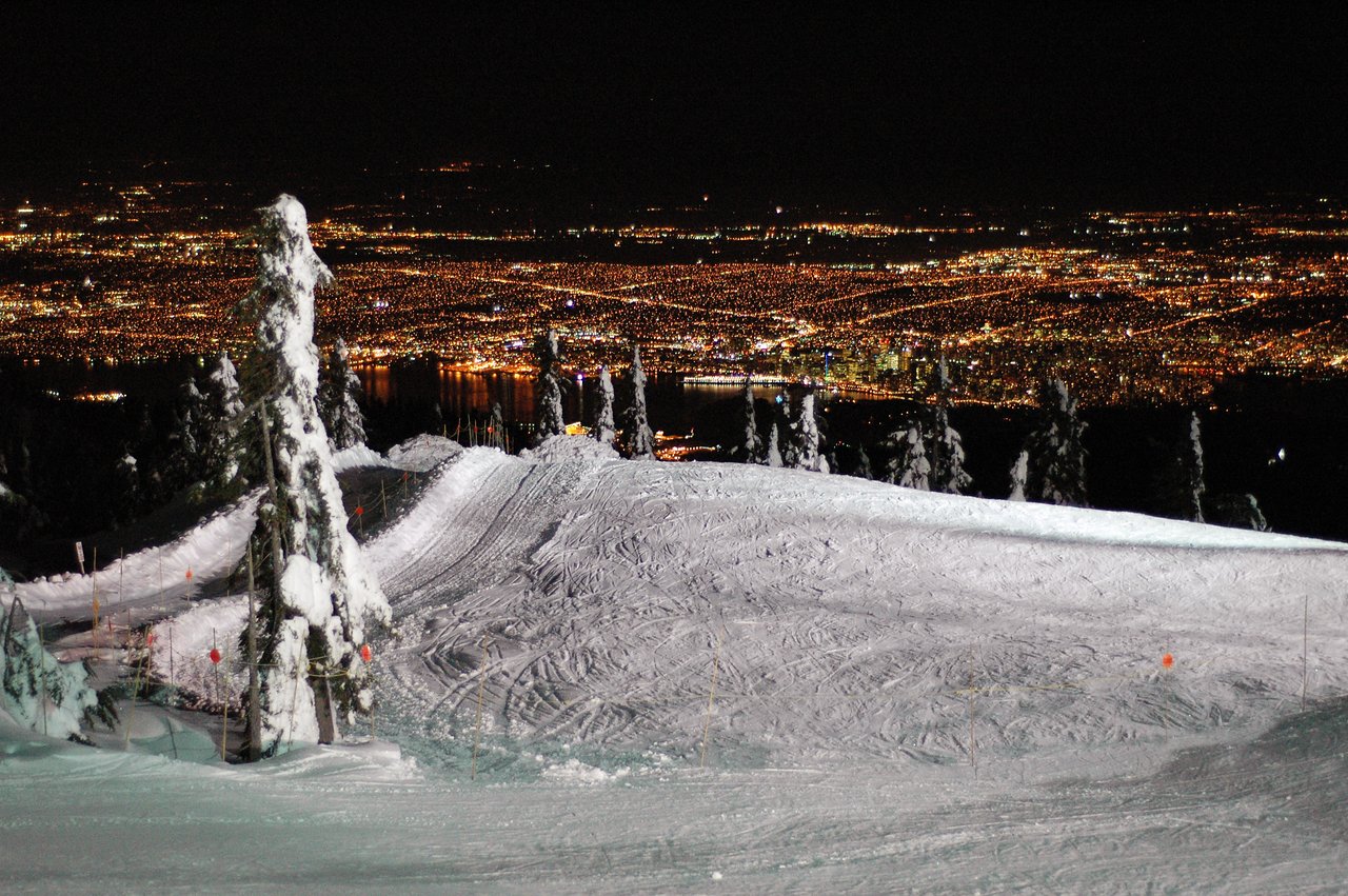 Snow-covered ski slope at night with city lights visible in the distance from Cypress Mountain, Vancouver.
