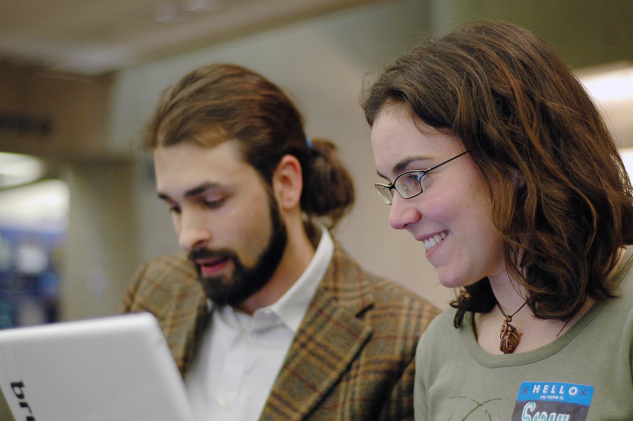 Two people working together on a laptop, focused and engaged in coding.