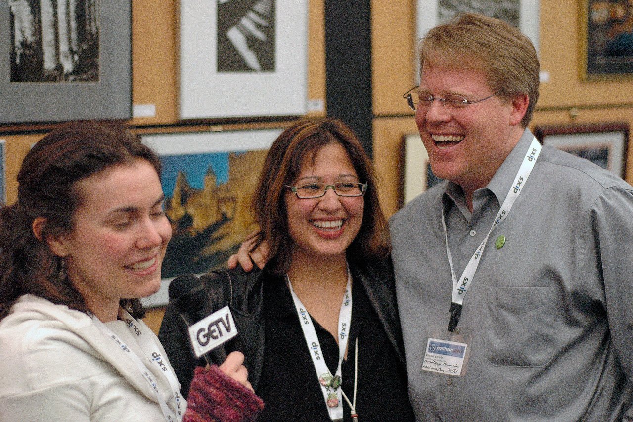 A woman interviews a smiling couple at an event, holding a microphone labeled "GETV.