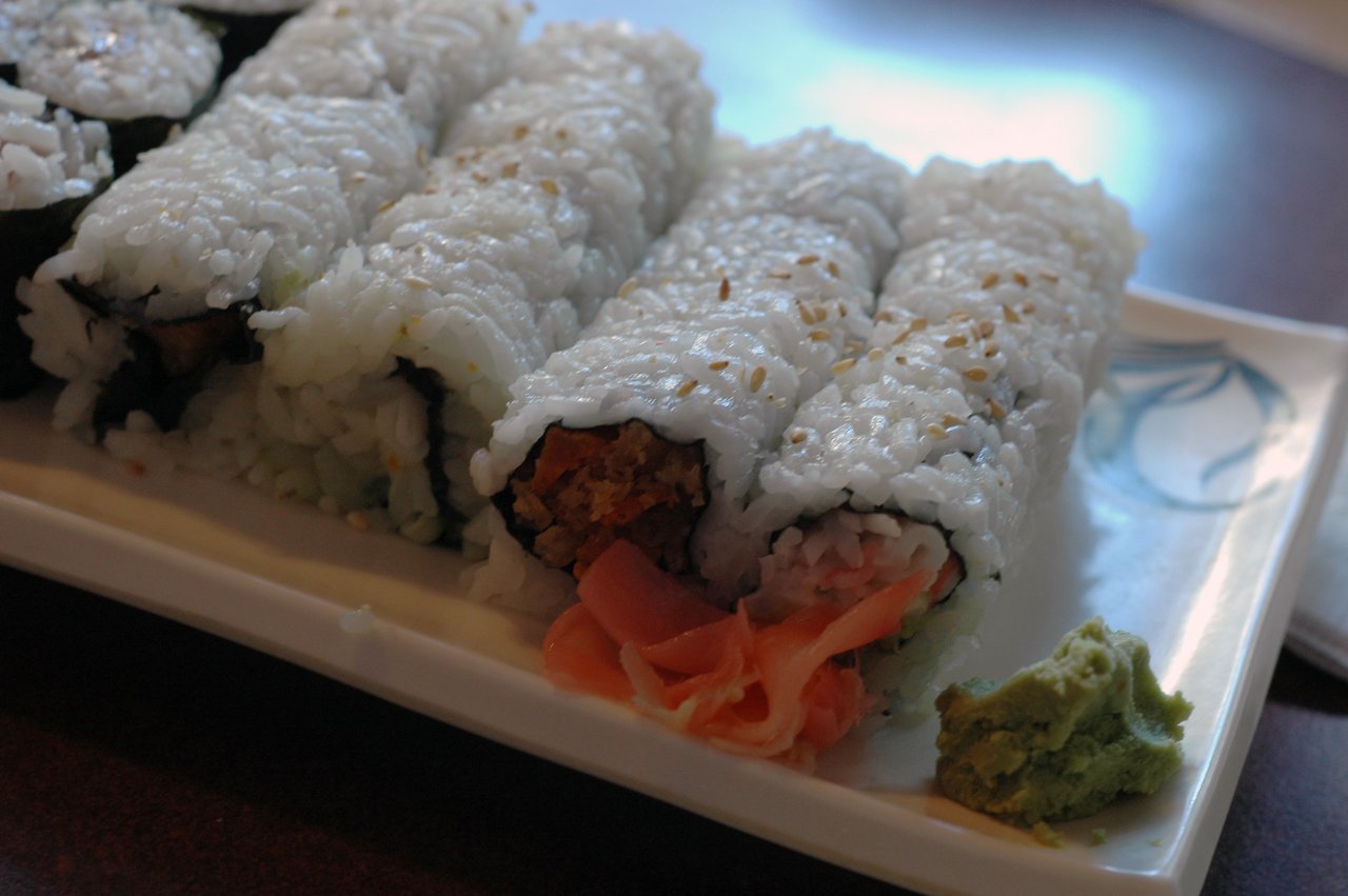 A plate of sushi rolls with white rice and sesame seeds, served with pickled ginger and wasabi on the side.