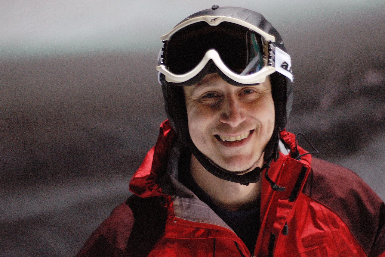 A person wearing a red jacket, ski goggles, and a helmet smiles while night skiing at Cypress Mountain.