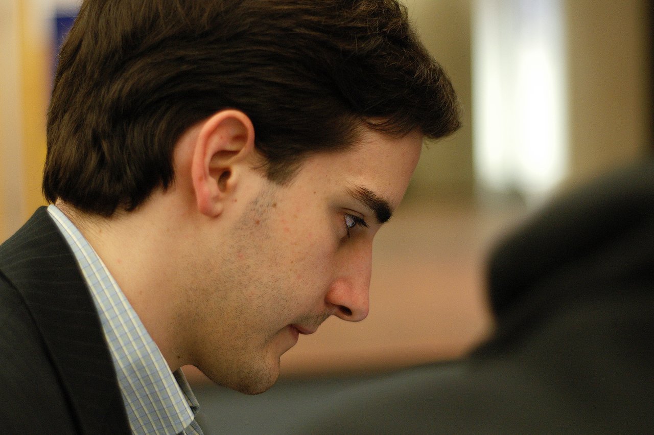 A man in a suit looks down with focus in an indoor setting.