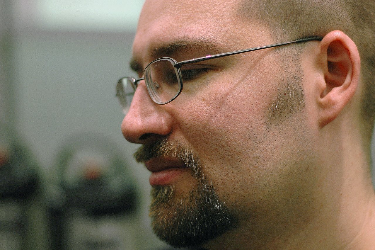 A close-up side profile of a man wearing glasses, looking to the left with a neutral expression.