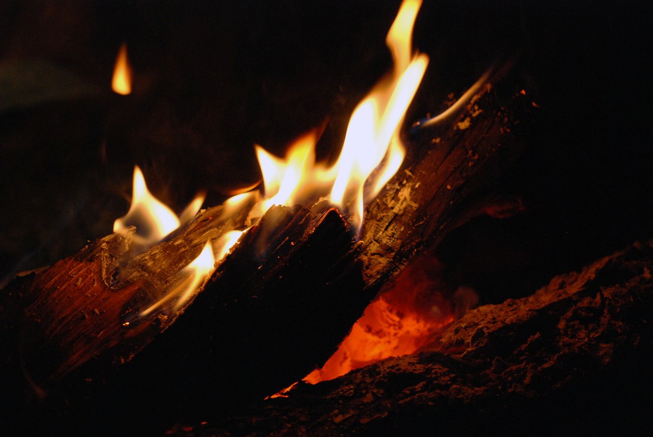 Burning logs with bright orange and yellow flames in a dark setting.