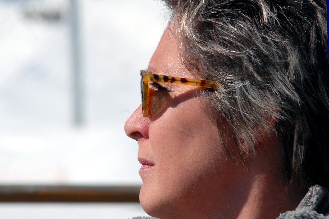 A person wearing tortoiseshell sunglasses looks into the distance with a neutral expression in a bright outdoor setting.