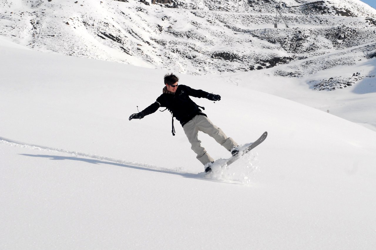 A person snowboards down a snowy slope, leaning to one side while kicking up powder.