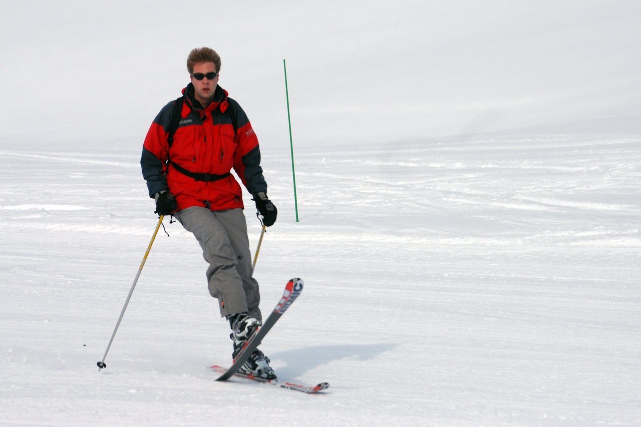 A person wearing a red jacket and sunglasses is skiing on a snowy slope, using ski poles for balance.