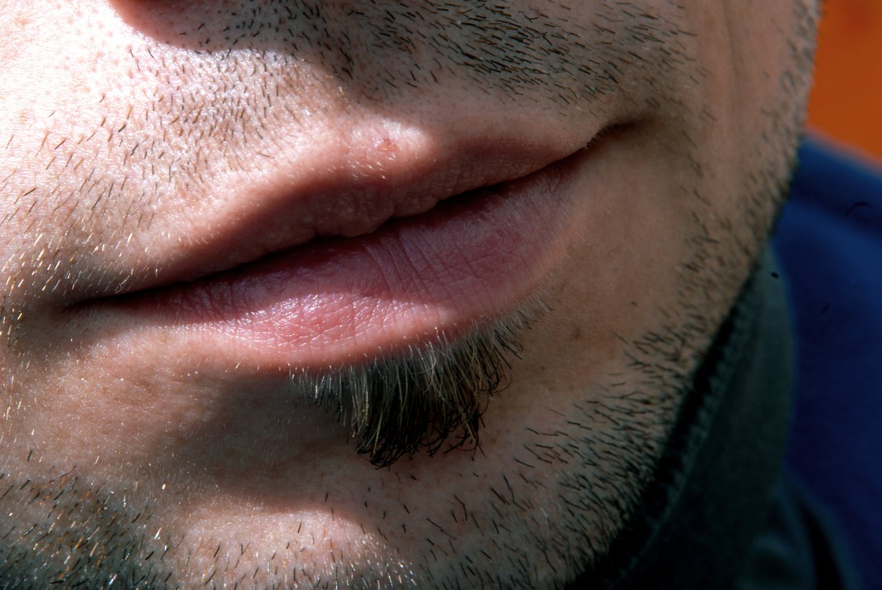 Close-up of a person's lips, chin, and facial hair with short stubble and a small goatee.