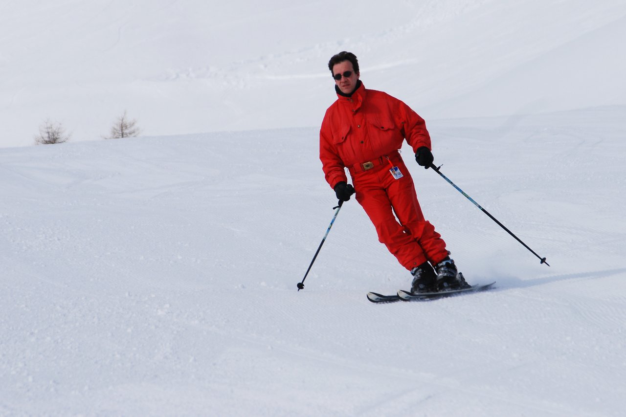 A person in a red ski suit is skiing downhill, using poles for balance on a snowy slope.