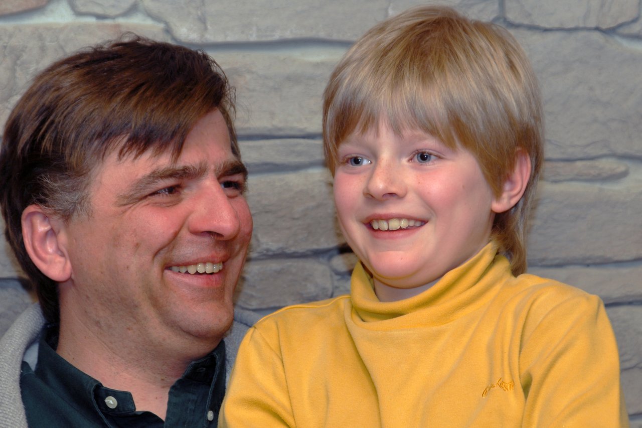 A man and a child smile together, looking happy.