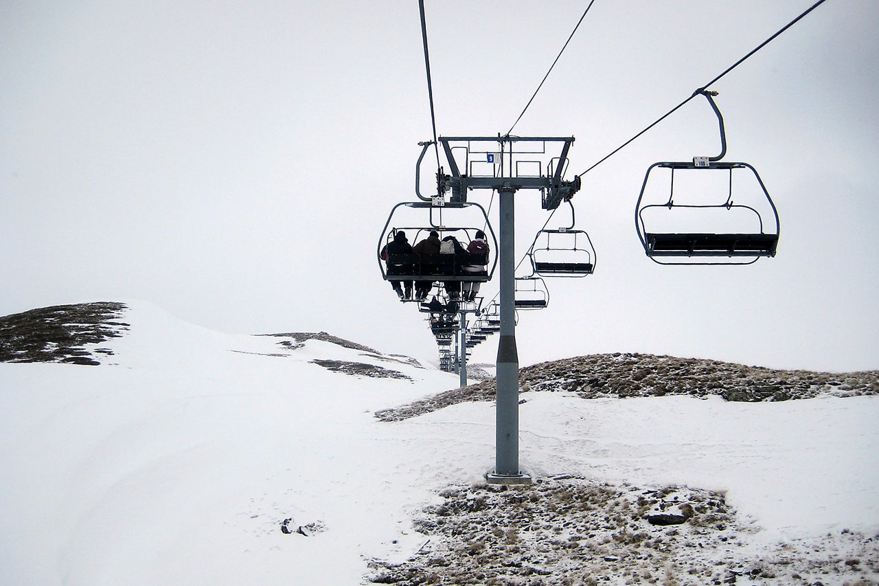 A ski lift carries people up a snowy mountain, with empty chairs visible on the side.