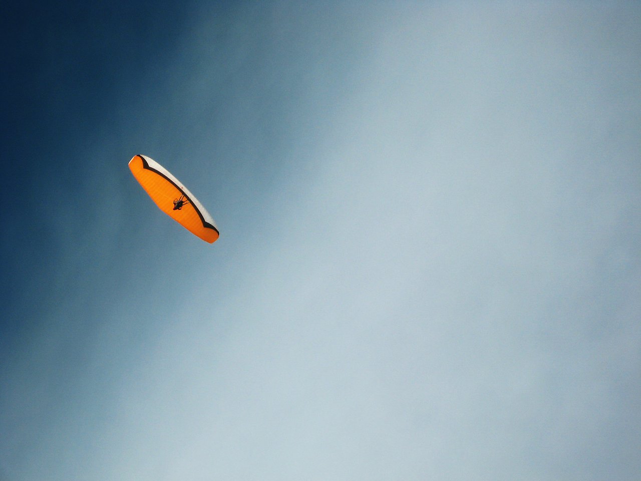 A person paraglides through the sky with an orange and white canopy.