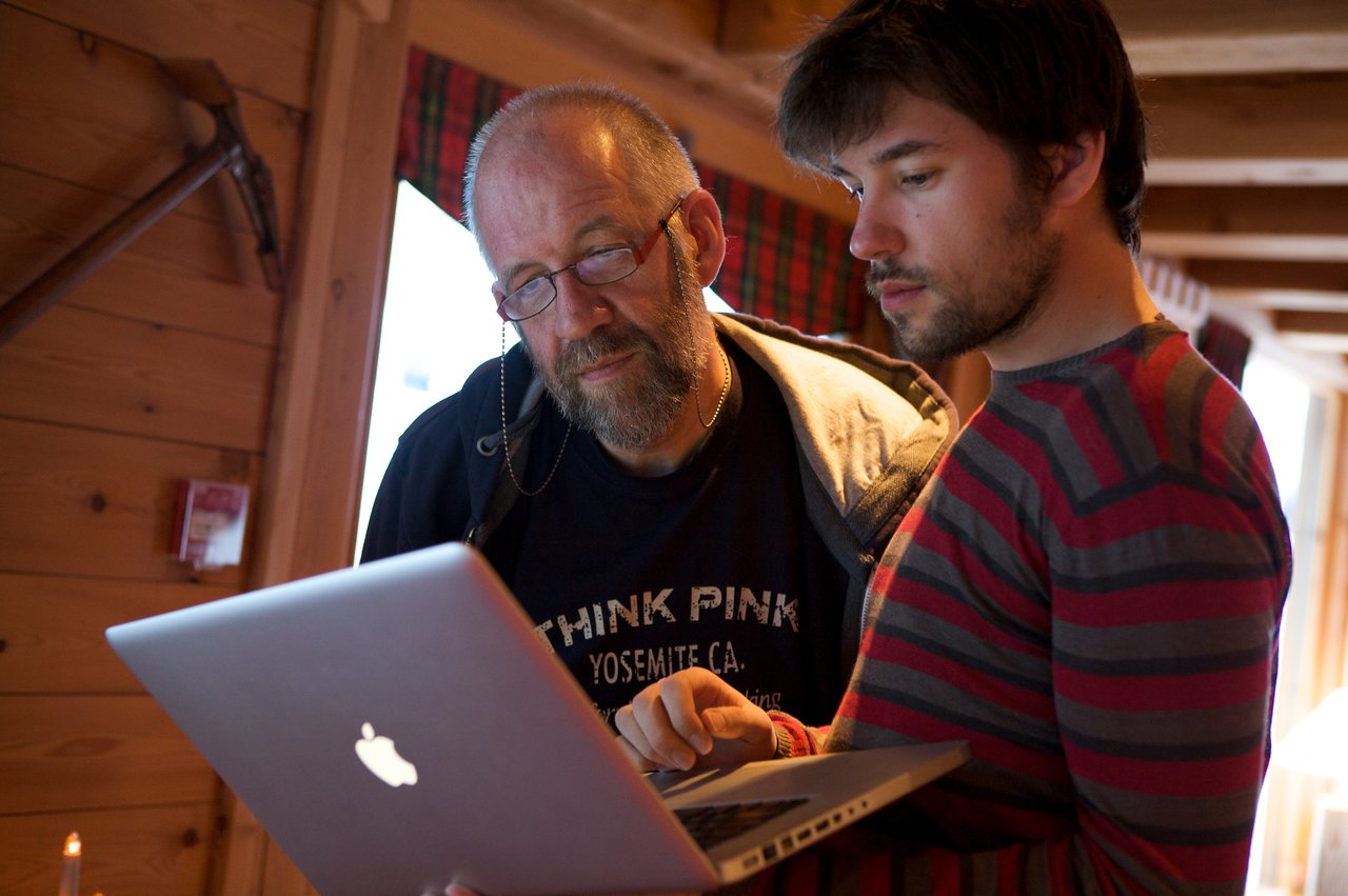 Two people looking at a laptop screen together, one pointing at something while the other observes closely.