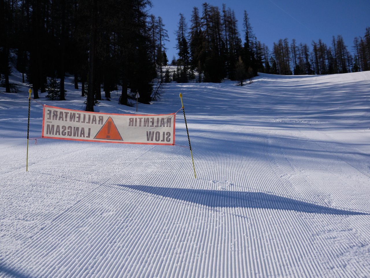 A warning sign on a snowy ski slope instructs skiers to slow down for safety.