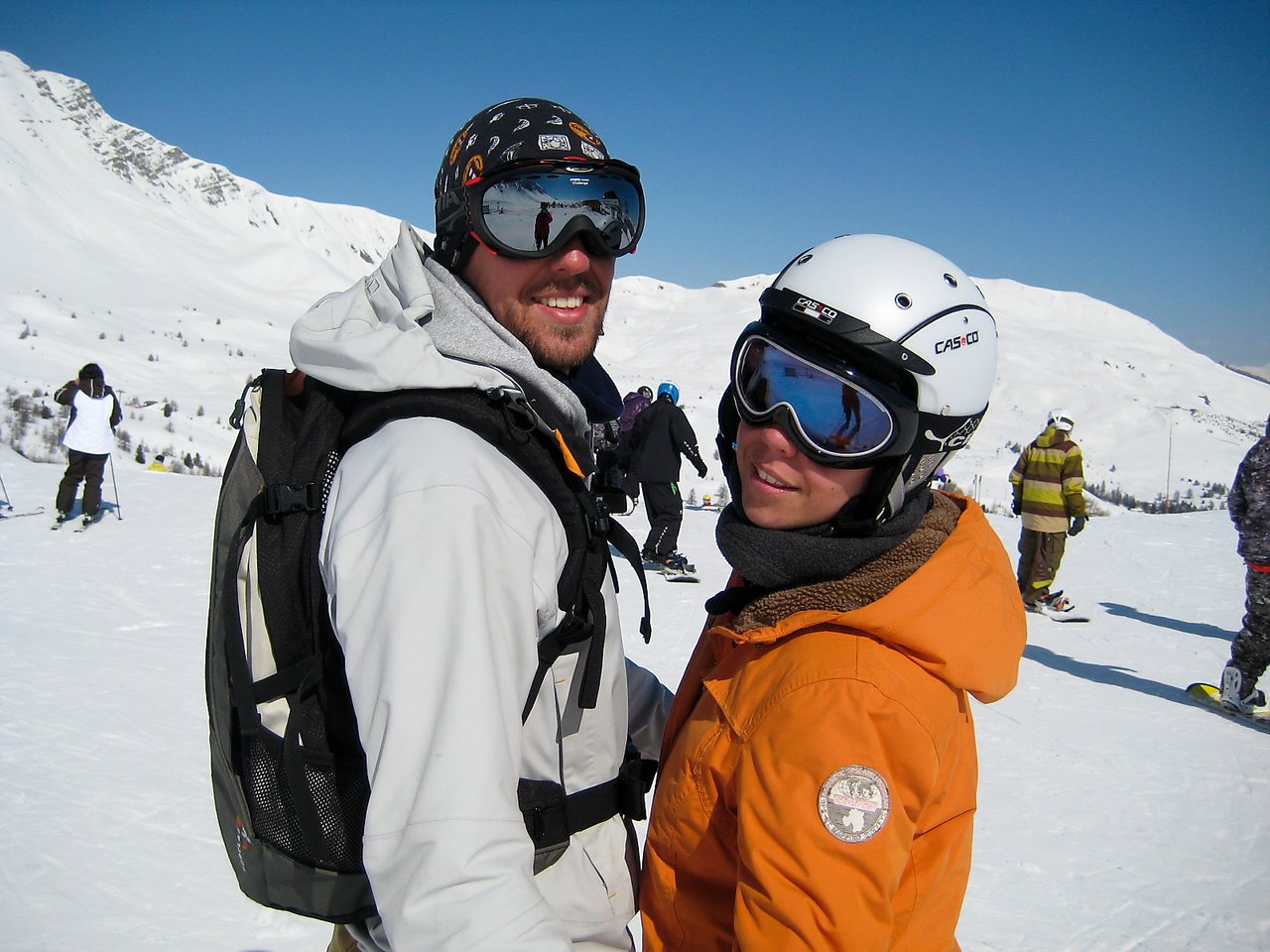 Two people in ski gear stand close together on a snowy mountain, smiling at the camera.