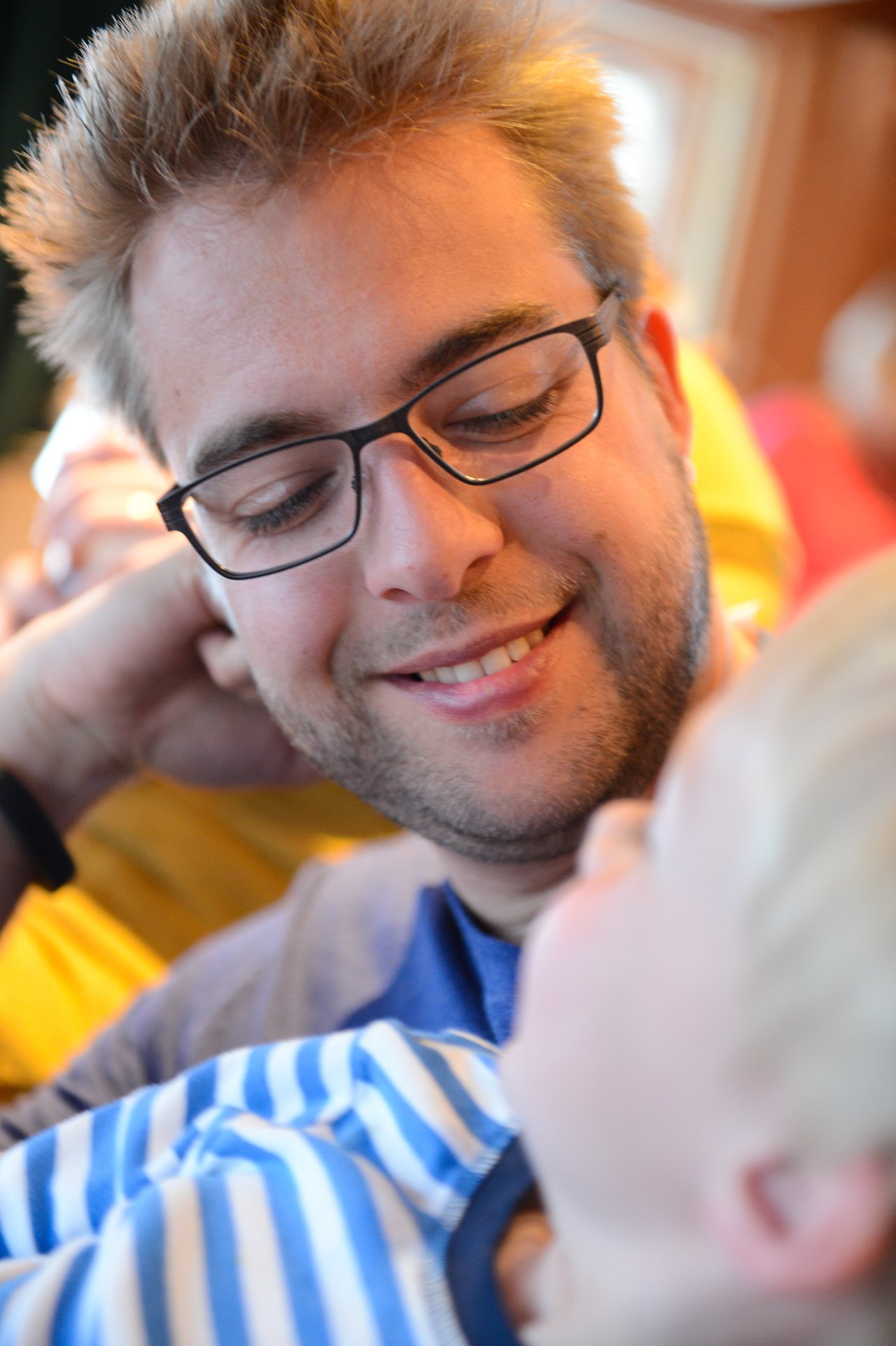 A man wearing glasses smiles while looking at a young child in his arms.