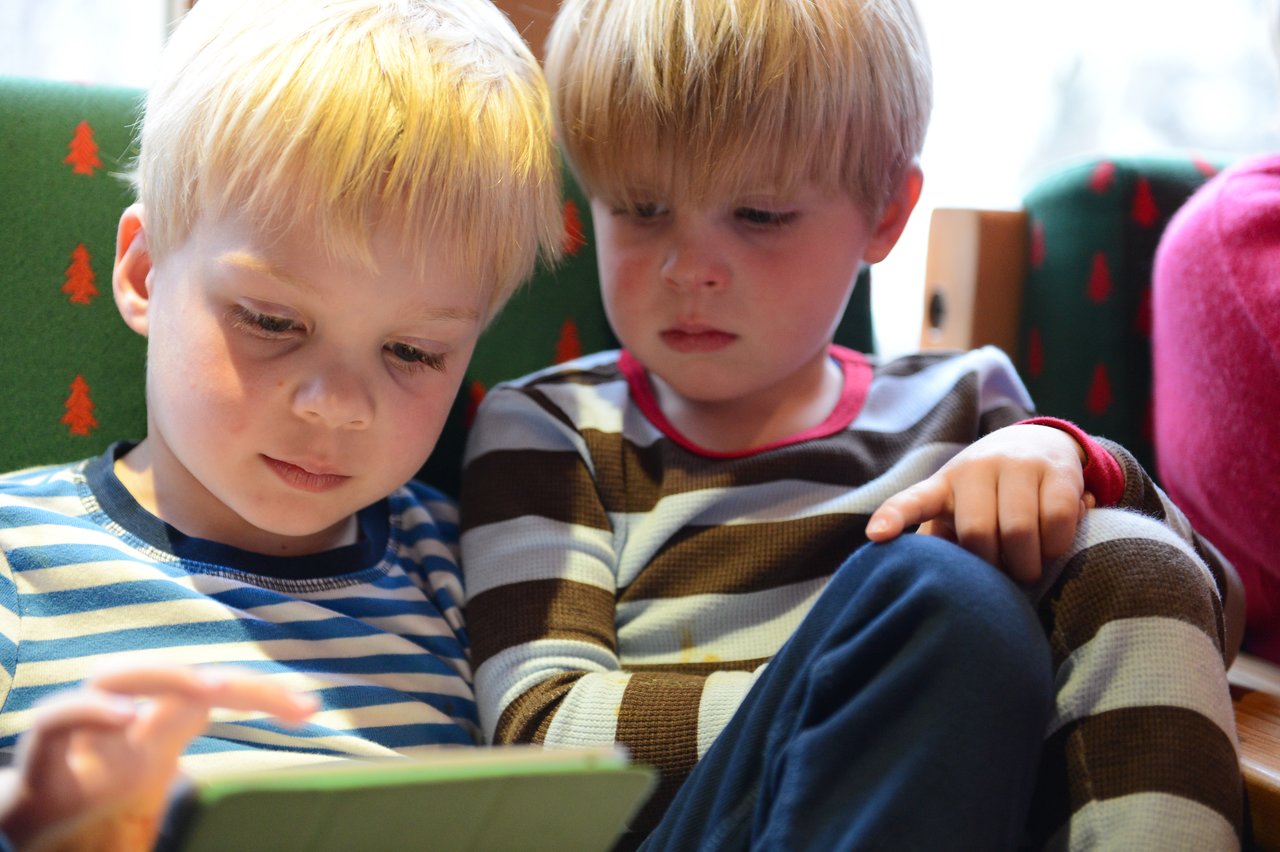 Two young boys in striped shirts sit closely together, looking at a tablet screen with focus.