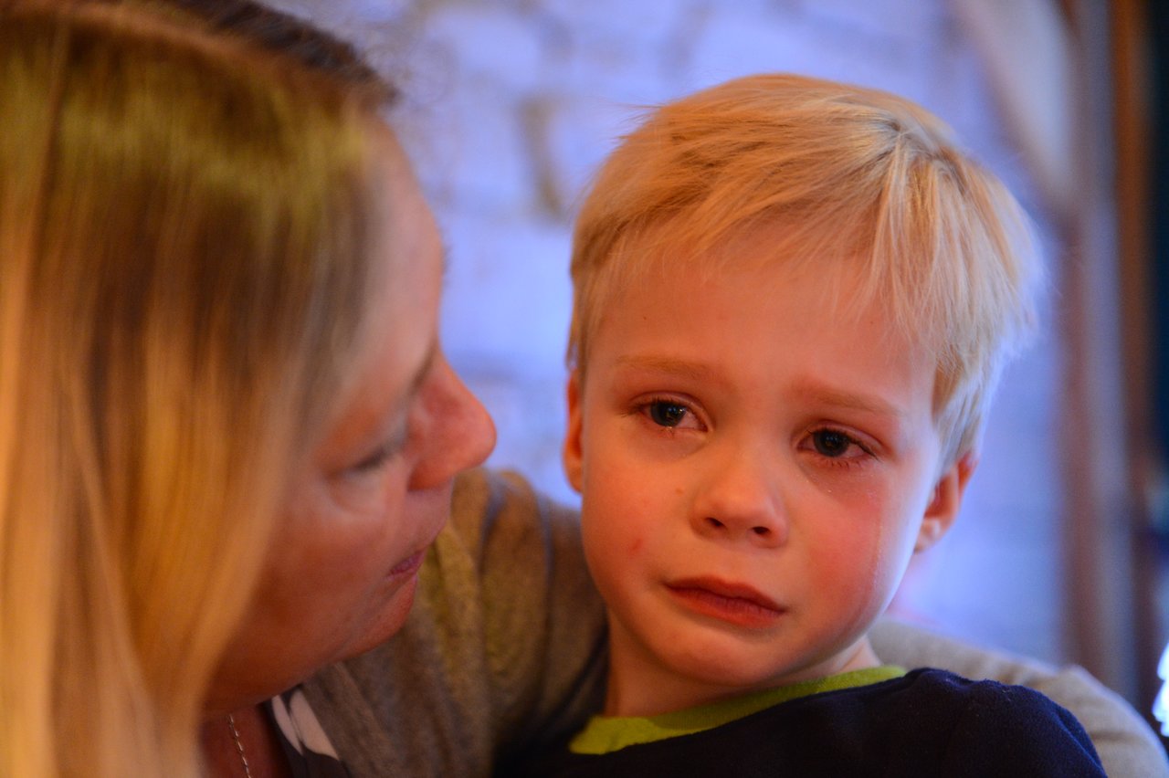 A young boy with teary eyes looks sad while an adult beside him offers comfort.